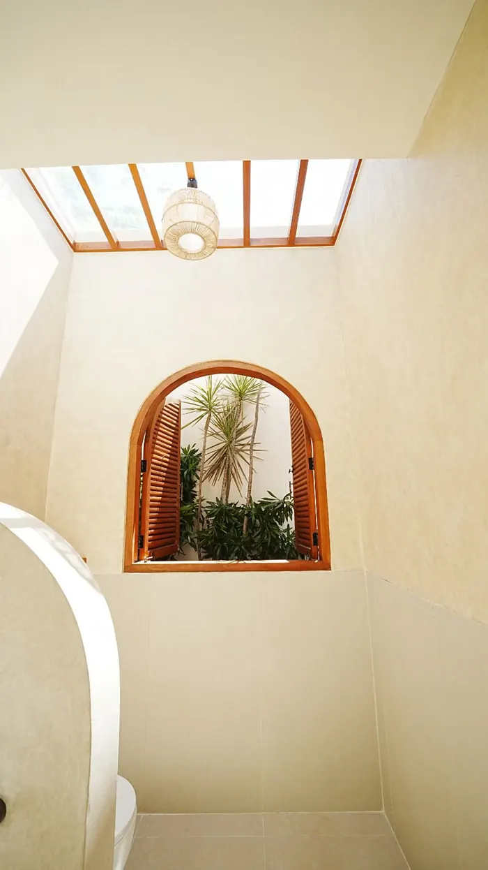 Arched window niche in cream plaster beneath a timber skylight in a Bali villa