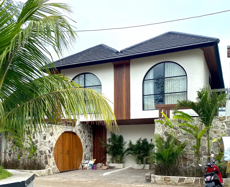 White two storey house in Bali with arched windows and a round timber door