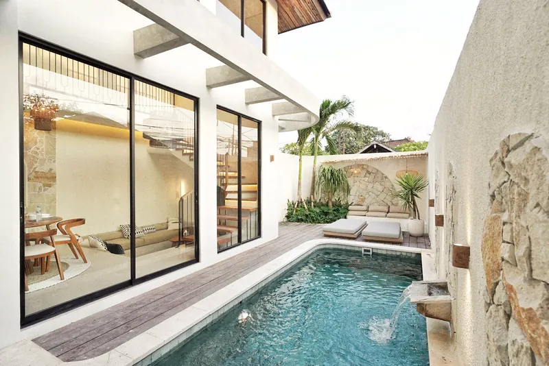 Narrow lap pool beside a cream villa with arched details and tall glass doors in Bali