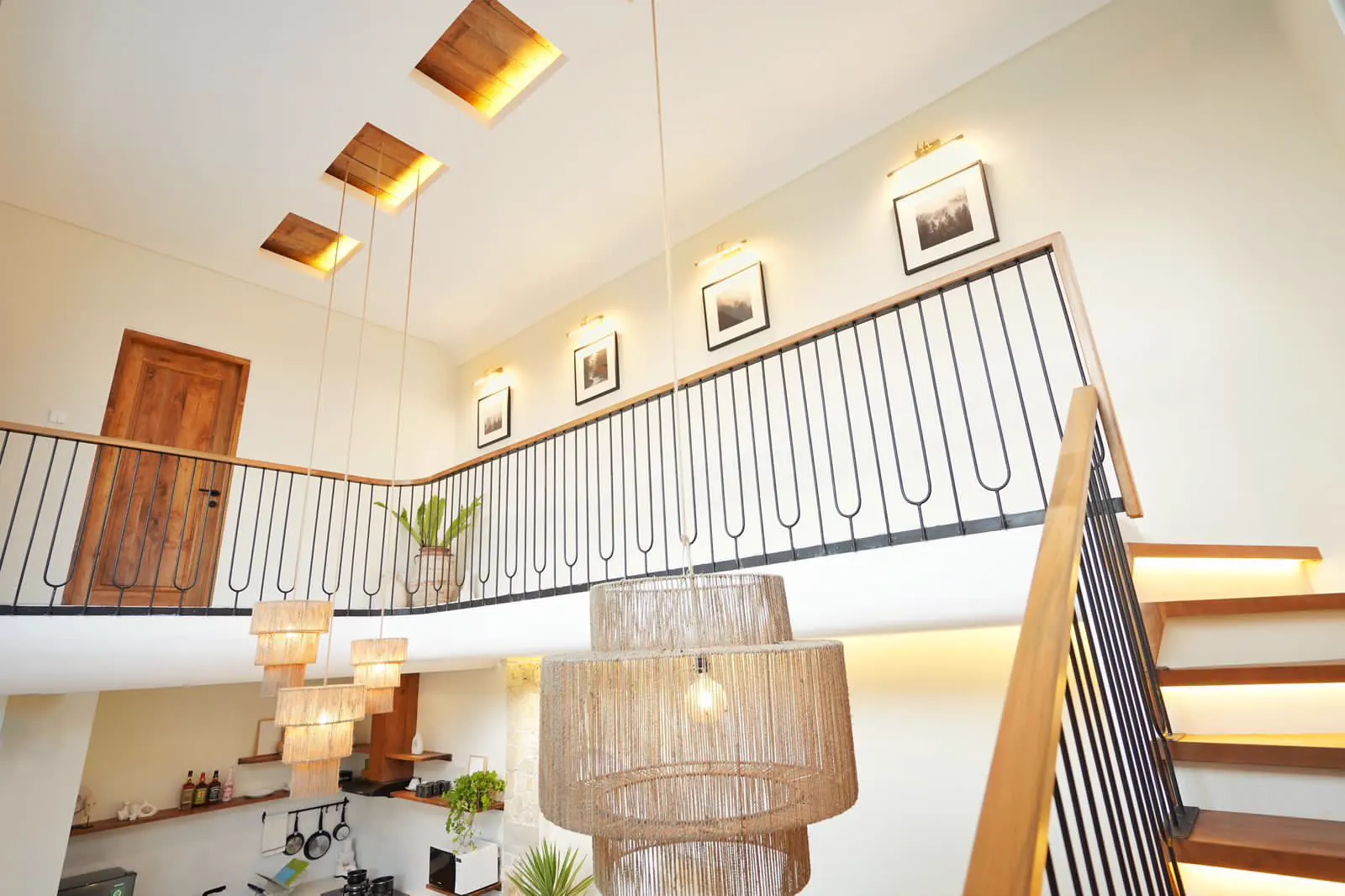 Double height villa hall in Bali with a timber staircase and woven rattan pendant lights