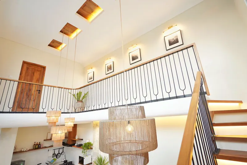 Double height villa hall in Bali with a timber staircase and woven rattan pendant lights